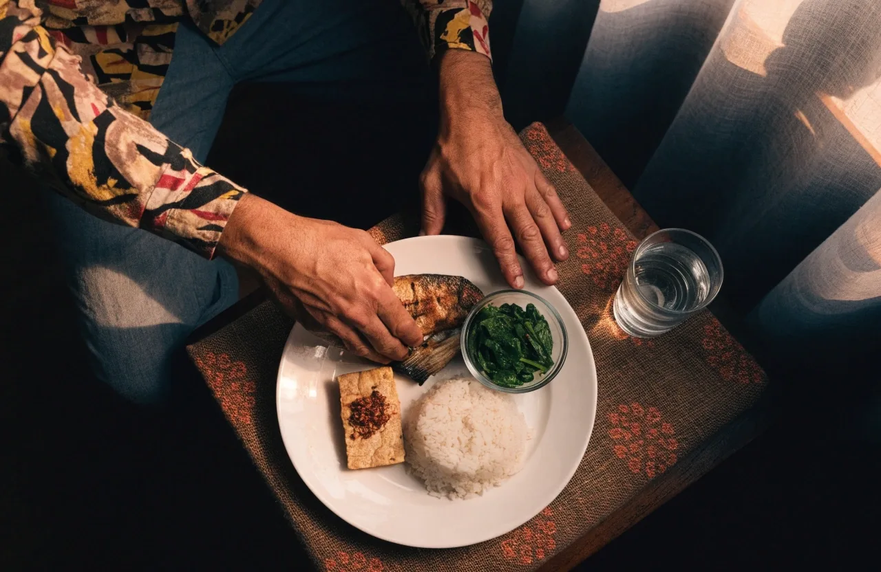 A Makassar man's dinner plate of rice, fish, tempeh and greens under warm evening light